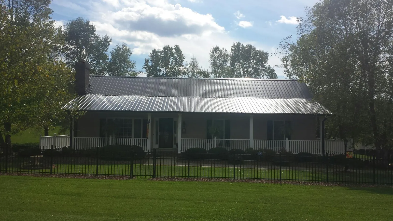 Gray metal roof on a brick ranch with a full width front porch — Gutter Guard Installation work by our crew in Lawrence