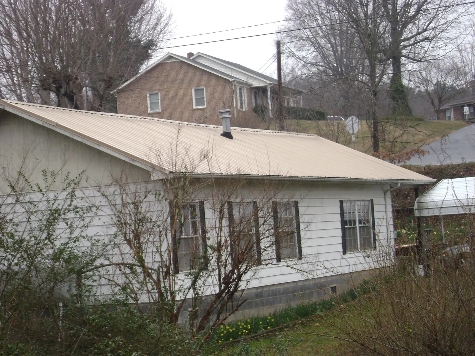 Tan metal roof on a white sided house set into a hillside — Commercial Roofing by Roofing Brothers in Lawrence